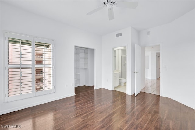 unfurnished bedroom with a spacious closet, visible vents, ensuite bathroom, and wood finished floors