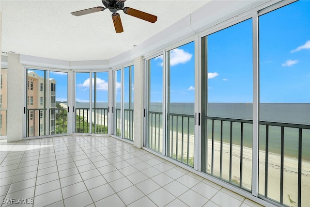 unfurnished sunroom featuring tile patterned flooring, a beach view, a healthy amount of sunlight, and a water view