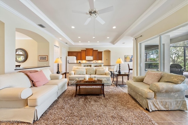 living room featuring light wood-type flooring, a raised ceiling, ceiling fan, and crown molding