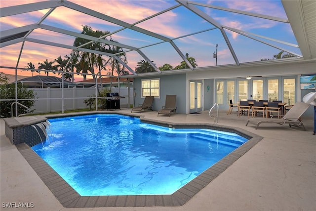 pool at dusk featuring a lanai, a patio area, pool water feature, and grilling area