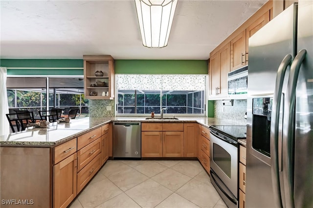 kitchen with kitchen peninsula, light stone counters, stainless steel appliances, sink, and light tile patterned flooring