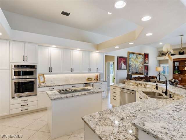 kitchen featuring light stone counters, white cabinets, sink, appliances with stainless steel finishes, and a center island