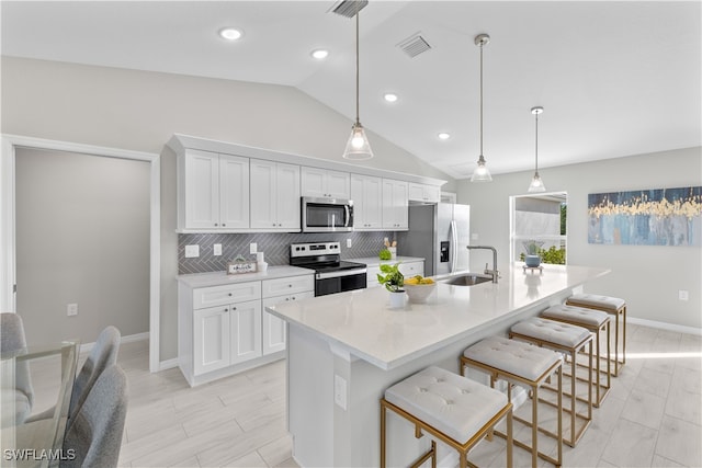 kitchen featuring sink, an island with sink, white cabinets, vaulted ceiling, and appliances with stainless steel finishes