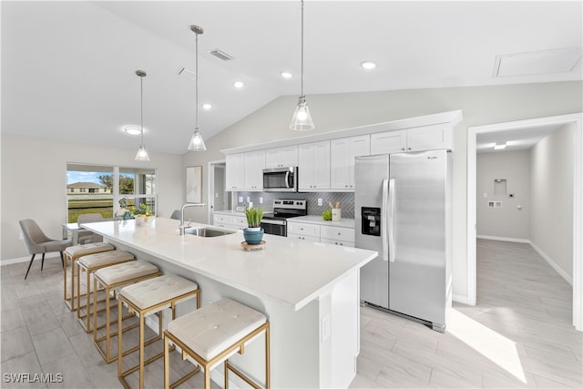 kitchen featuring a kitchen breakfast bar, white cabinets, stainless steel appliances, a center island with sink, and sink