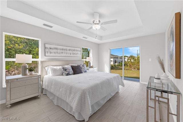 bedroom with multiple windows, a raised ceiling, access to exterior, and ceiling fan