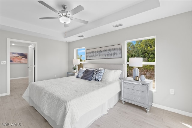 bedroom featuring ceiling fan, a raised ceiling, light wood-type flooring, and multiple windows