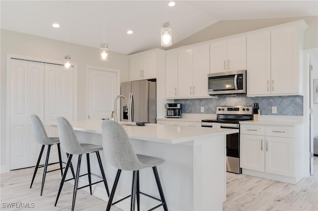 kitchen featuring stainless steel appliances, vaulted ceiling, a kitchen island with sink, white cabinets, and hanging light fixtures