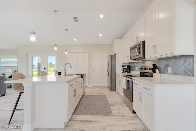 kitchen with pendant lighting, a center island with sink, light hardwood / wood-style floors, white cabinetry, and stainless steel appliances