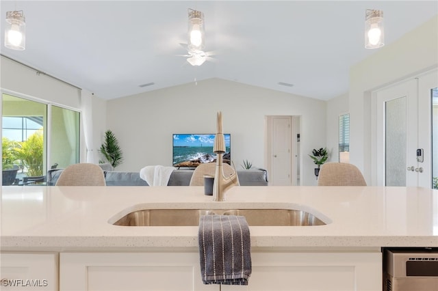 kitchen with pendant lighting, lofted ceiling, white cabinets, sink, and light stone countertops