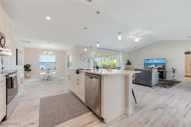 kitchen with white cabinetry, hanging light fixtures, an island with sink, appliances with stainless steel finishes, and light wood-type flooring