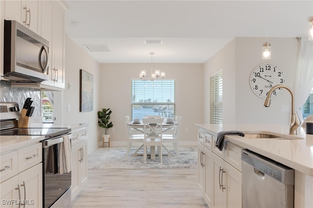 kitchen featuring light wood-type flooring, stainless steel appliances, decorative light fixtures, white cabinets, and a chandelier