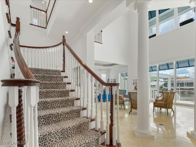 stairs with decorative columns, ornamental molding, a high ceiling, and a wealth of natural light