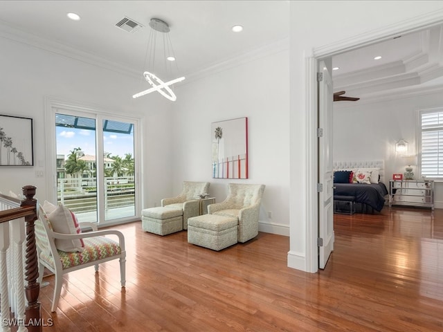 sitting room with a wealth of natural light, crown molding, wood-type flooring, and ceiling fan with notable chandelier