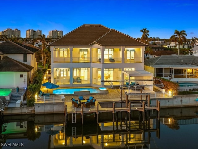 back house at dusk featuring a patio, a pool with hot tub, and a balcony