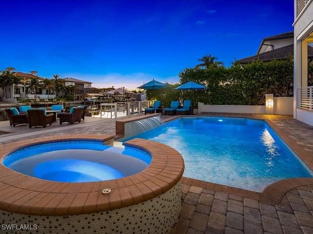 pool at dusk featuring a patio, pool water feature, and an in ground hot tub