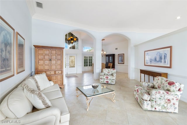 tiled living room with crown molding, a high ceiling, and an inviting chandelier