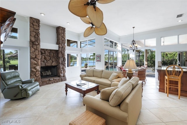 tiled living room featuring ceiling fan with notable chandelier, a fireplace, crown molding, and a towering ceiling