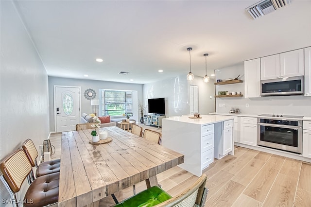 kitchen featuring appliances with stainless steel finishes, white cabinetry, a kitchen island, pendant lighting, and light wood-type flooring