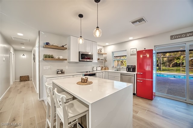 kitchen with appliances with stainless steel finishes, light hardwood / wood-style floors, white cabinets, pendant lighting, and a kitchen bar