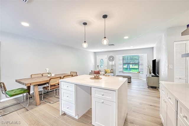 kitchen with white cabinets, decorative light fixtures, light wood-type flooring, and a center island