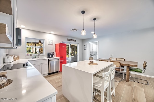 kitchen featuring light hardwood / wood-style floors, white cabinets, decorative light fixtures, stainless steel dishwasher, and sink