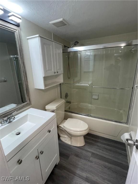 bathroom with visible vents, toilet, enclosed tub / shower combo, vanity, and wood finished floors