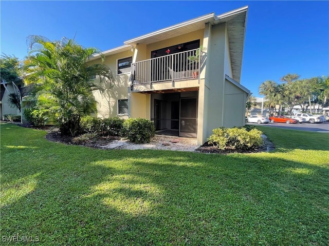 back of property with a lawn, a balcony, and stucco siding