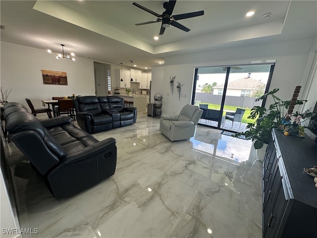 living room with a raised ceiling and ceiling fan with notable chandelier