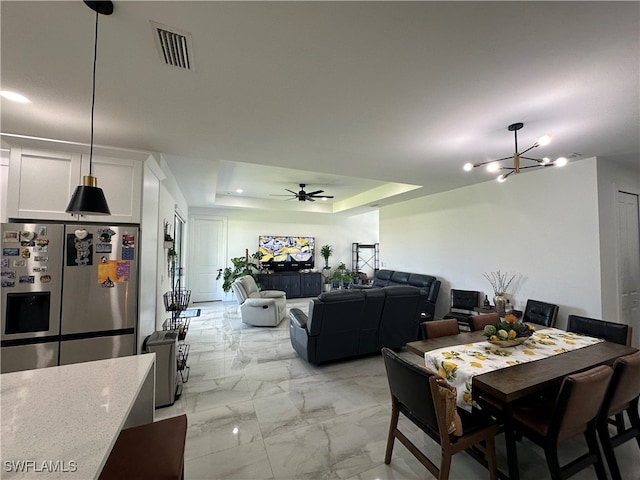 dining area featuring ceiling fan with notable chandelier and a raised ceiling