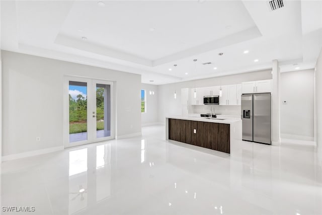 kitchen with white cabinets, stainless steel appliances, a center island with sink, and a tray ceiling