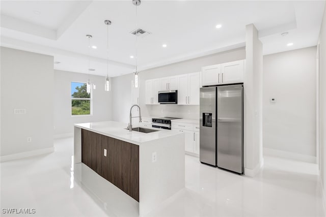 kitchen featuring stainless steel appliances, a tray ceiling, sink, a center island with sink, and white cabinetry