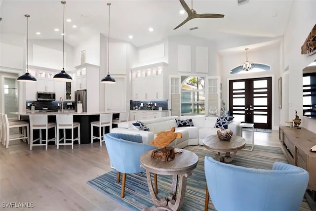 living room with high vaulted ceiling, wood-type flooring, ceiling fan, french doors, and sink