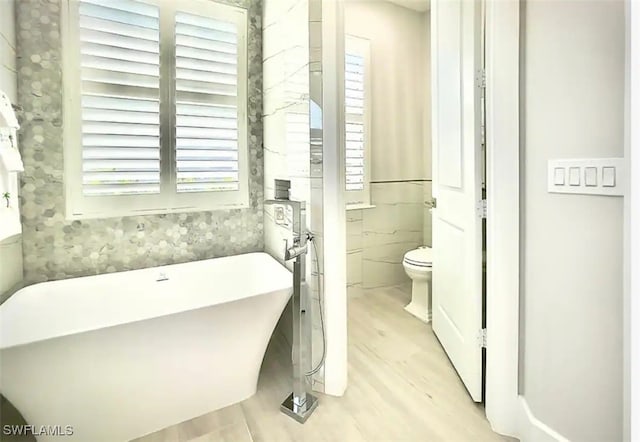 bathroom with tile walls, hardwood / wood-style flooring, a washtub, and toilet