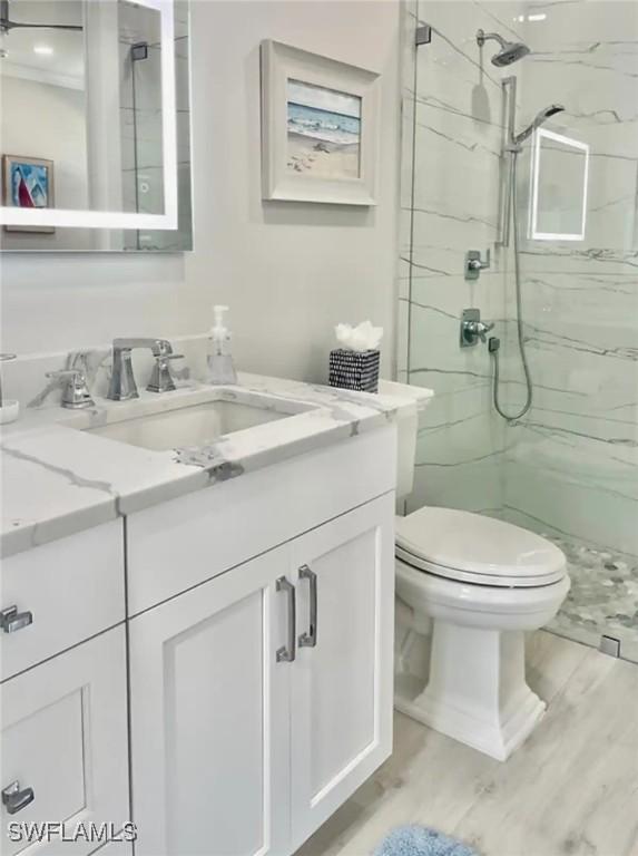 bathroom with hardwood / wood-style floors, vanity, toilet, and a shower with door