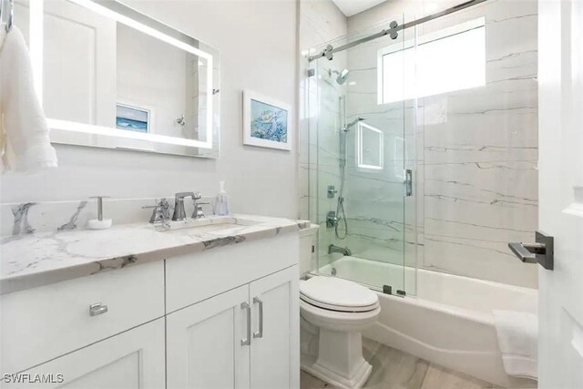 full bathroom with enclosed tub / shower combo, vanity, and toilet