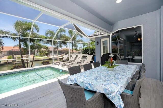 view of pool featuring glass enclosure, a water view, and a patio area