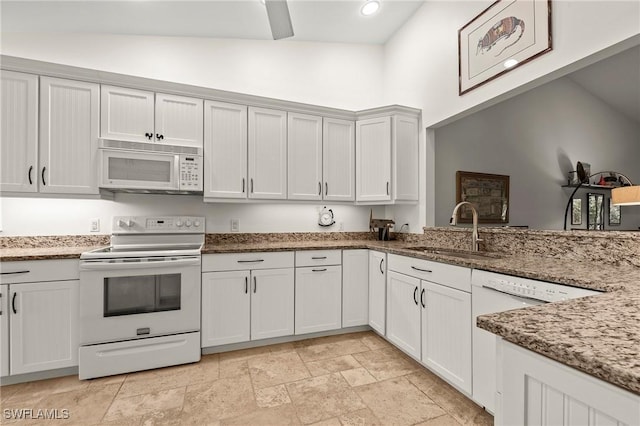 kitchen featuring white appliances, lofted ceiling, white cabinetry, sink, and light stone counters