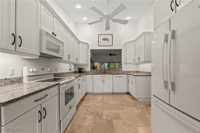 kitchen with white appliances, white cabinets, sink, stone countertops, and ceiling fan