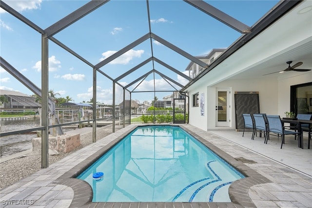 view of pool featuring ceiling fan, glass enclosure, a water view, and a patio area