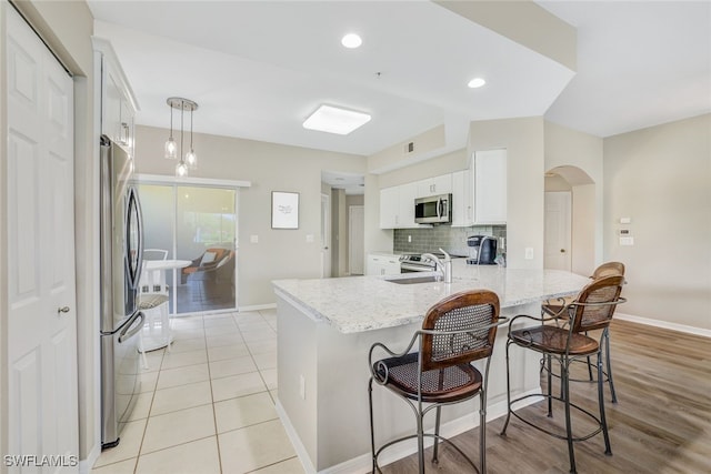 kitchen featuring white cabinetry, kitchen peninsula, appliances with stainless steel finishes, decorative light fixtures, and light stone countertops