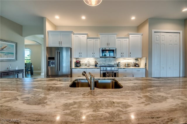 kitchen with white cabinetry, backsplash, light stone countertops, stainless steel appliances, and sink