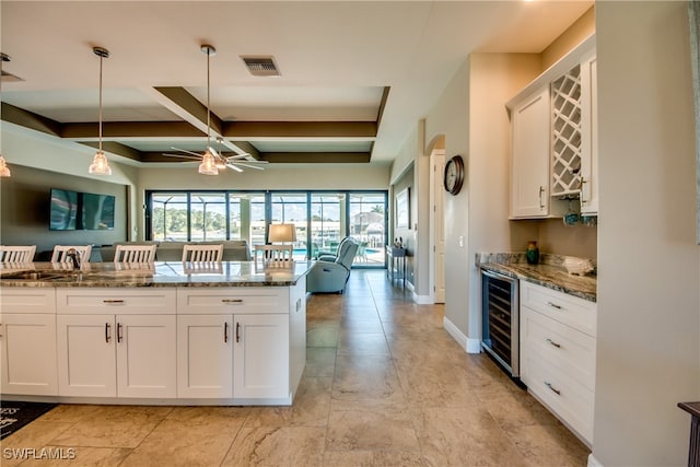 kitchen with white cabinets, beverage cooler, hanging light fixtures, ceiling fan, and stone countertops