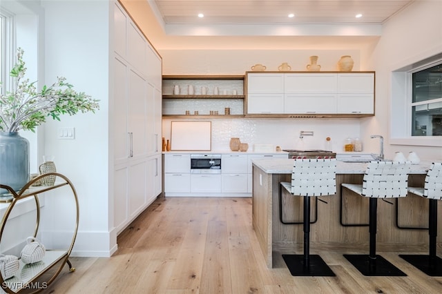 kitchen with light hardwood / wood-style flooring, white cabinetry, wooden ceiling, light stone countertops, and a kitchen bar