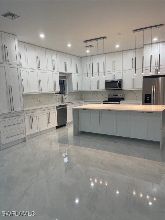 kitchen with sink, white cabinets, backsplash, appliances with stainless steel finishes, and decorative light fixtures