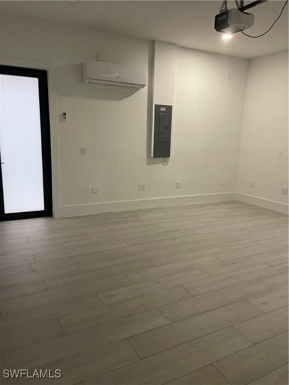 unfurnished room with light wood finished floors, electric panel, baseboards, and an AC wall unit