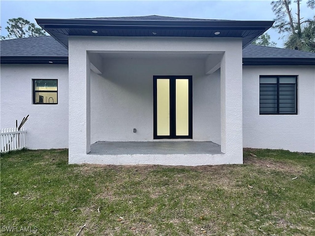 back of property with a shingled roof, a yard, fence, and stucco siding