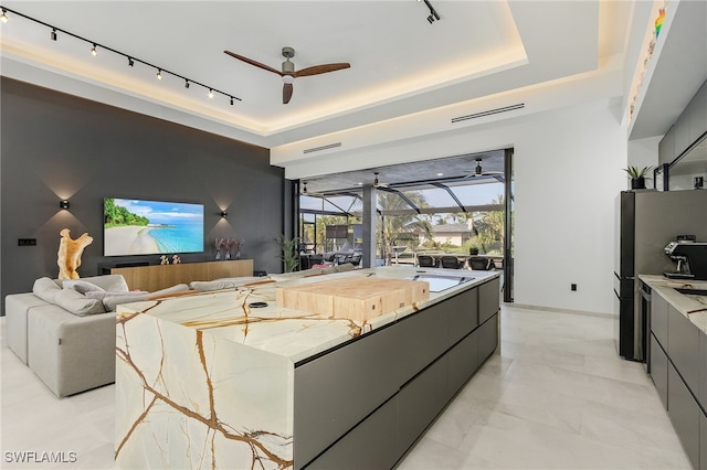 interior space with a tray ceiling, gray cabinets, rail lighting, and ceiling fan