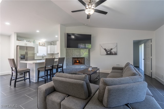 living room featuring ceiling fan, a tile fireplace, sink, and vaulted ceiling