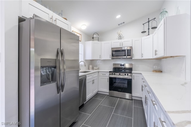 kitchen featuring stainless steel appliances, white cabinetry, sink, light stone countertops, and backsplash