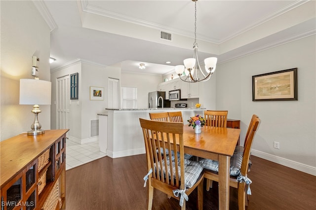 dining space with a tray ceiling, sink, a notable chandelier, dark hardwood / wood-style flooring, and ornamental molding